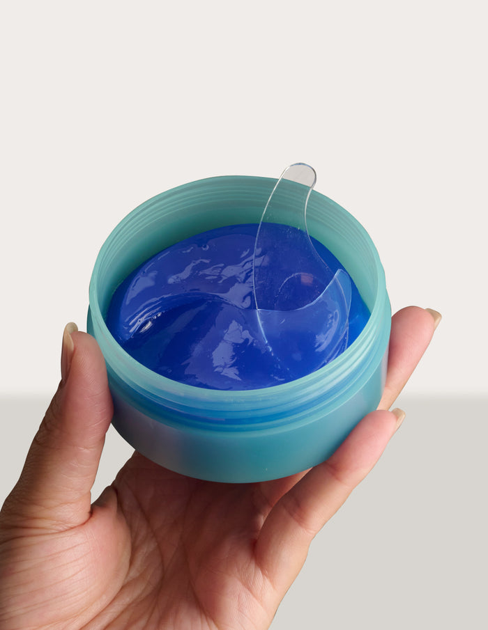 Hand holding an open teal jar of blue gel with a clear spatula