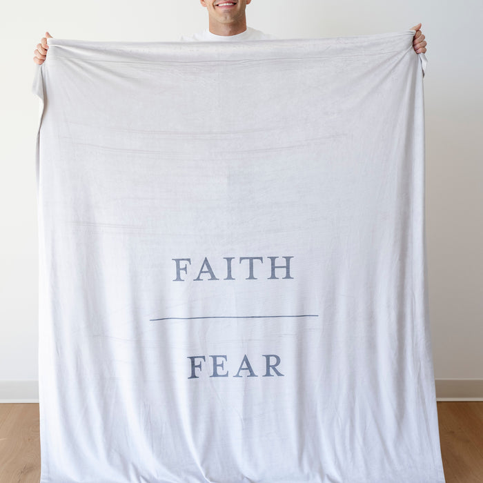 Person holding a gray Christian blanket featuring the words "Faith Over Fear," faith-inspired throw blanket offering comfort, encouragement, and a reminder to trust God through life's challenges.