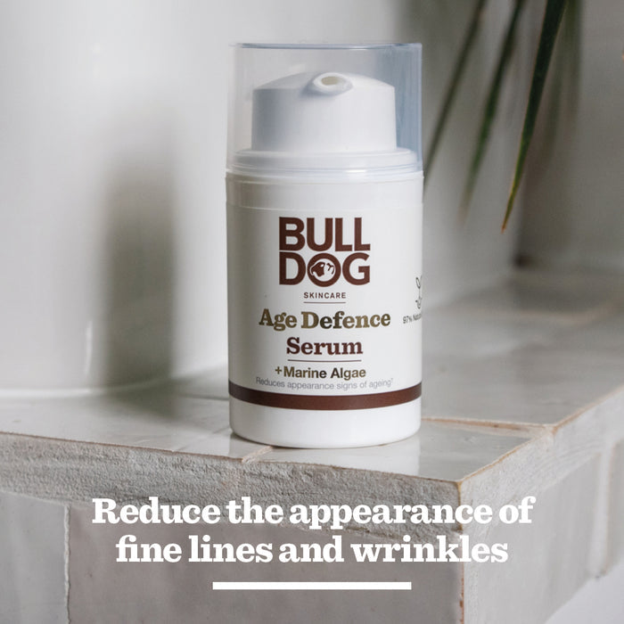 A bottle of Age Defence Serum rests on a tiled surface. Text below says, Reduce the appearance of fine lines and wrinkles with natural origin ingredients.