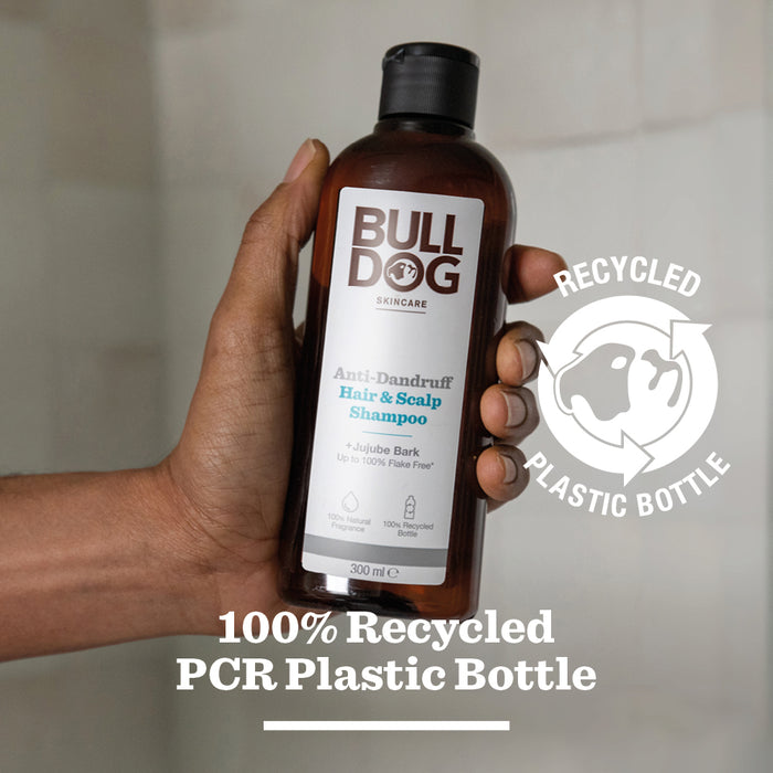A hand holds a brown bottle of Anti-Dandruff Shampoo. Text notes the bottle is made from 100% recycled plastic, shown with a recycled plastic icon.