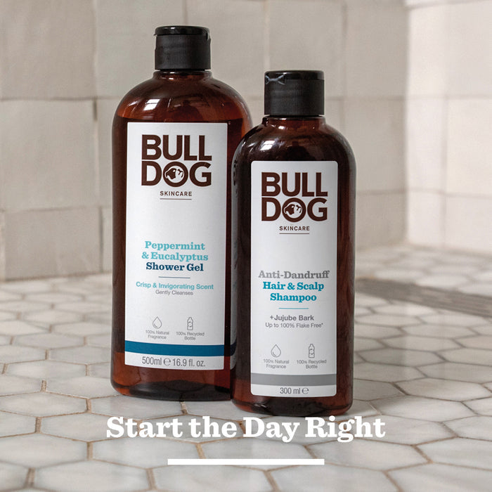 Two brown bottles of Bulldog Skincare—a Peppermint & Eucalyptus Shower Gel and an Anti-Dandruff Shampoo—stand on white hexagon tiles with “Start the Day Right” text below.