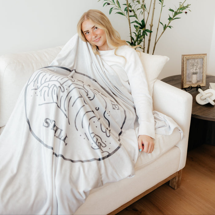 Woman relaxing with a Christian blanket featuring the Be Still scripture design, wrapped in a soft faith-inspired throw blanket.