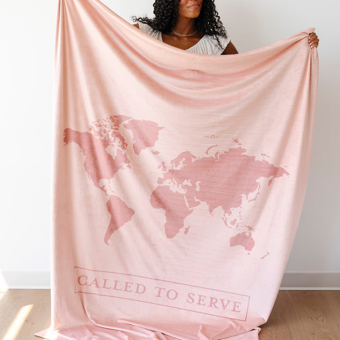 Woman holding a blush pink LDS missionary blanket featuring a world map design and the words "Called to Serve," meaningful missionary gift blanket celebrating faith, service, and missionary journeys around the world.