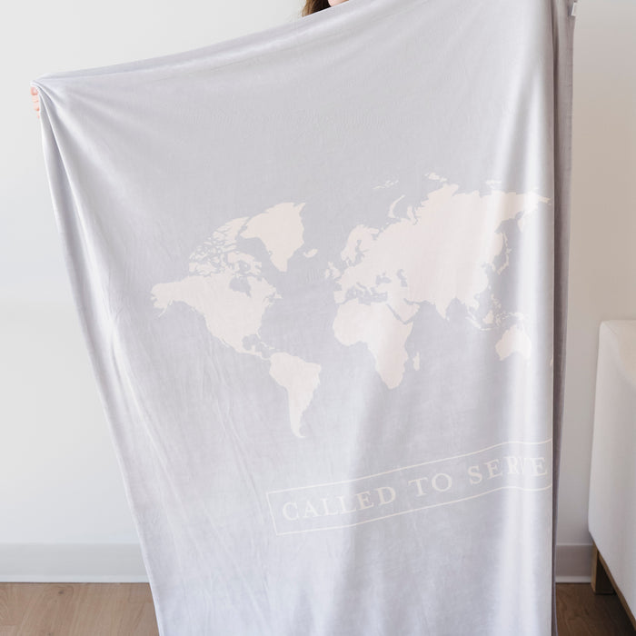 Person holding a glacier blue LDS missionary blanket featuring a world map design and the words "Called to Serve," meaningful missionary gift blanket celebrating faith, service, and missionary journeys around the world.