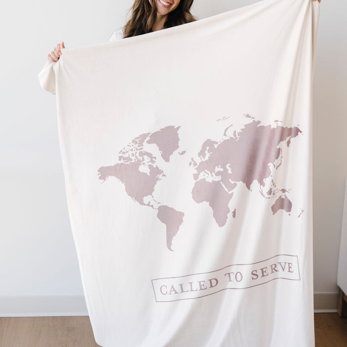Woman holding a shell cream LDS missionary blanket featuring a world map design and the words "Called to Serve," meaningful missionary gift blanket celebrating faith, service, and missionary journeys around the world.
