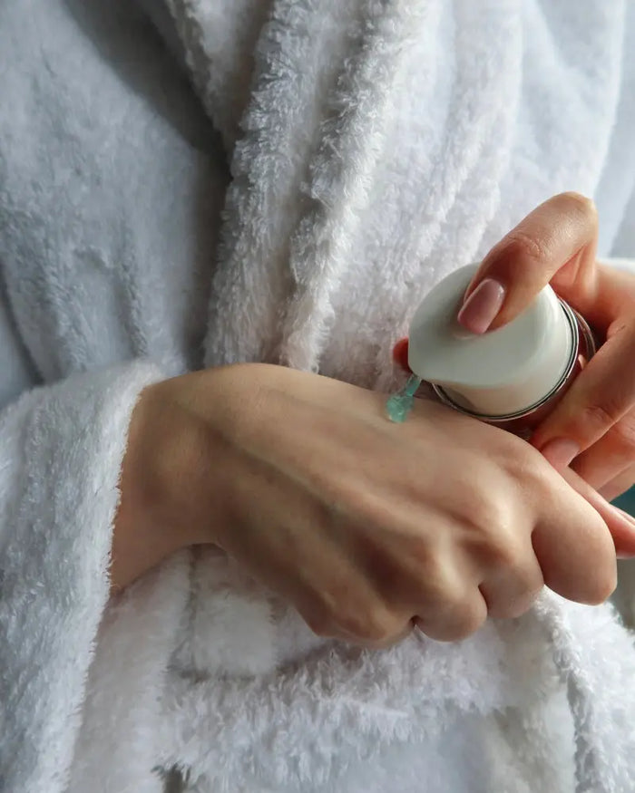 Person applying a skincare product to their wrist with a small container.