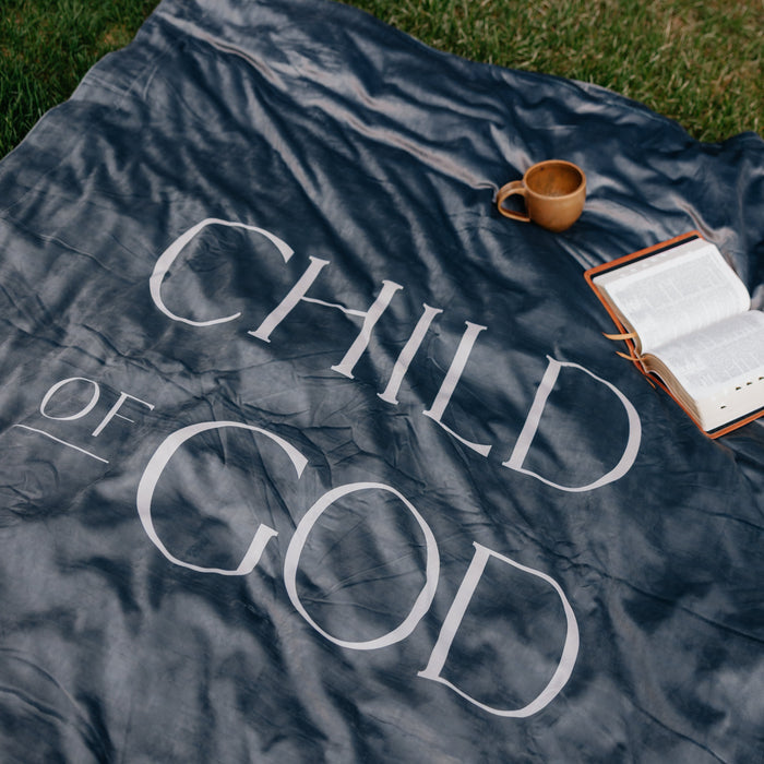 Dark obsidian Christian blanket featuring the words "Child of God" displayed outdoors with an open Bible and mug, faith-inspired throw blanket for comfort and reflection.