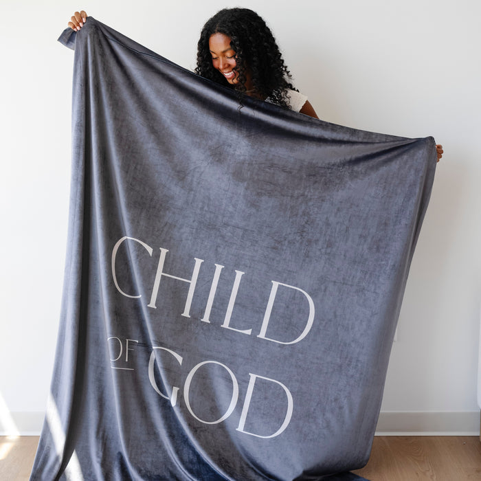 Person holding a dark obsidian Christian blanket featuring the words "Child of God," soft faith-inspired throw blanket displayed against a neutral background.