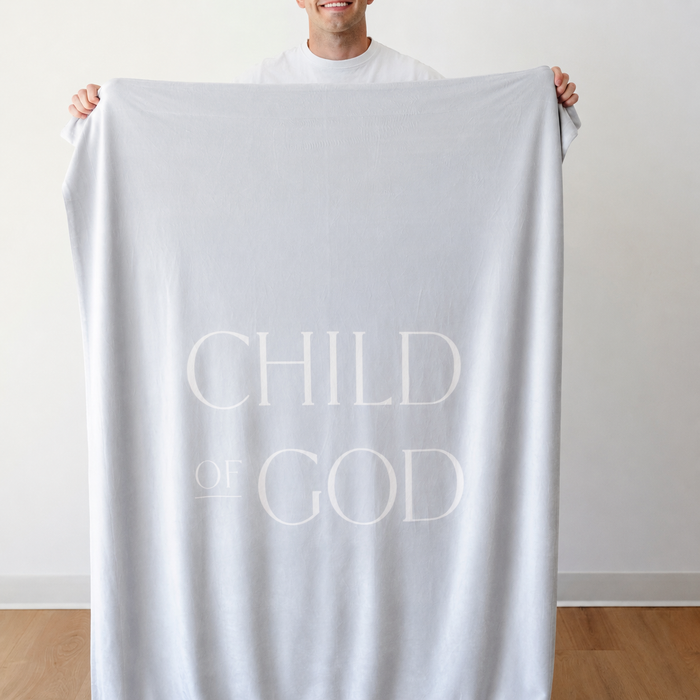Person holding a light glacier blue Christian blanket featuring the words "Child of God," soft faith-inspired throw blanket displayed against a neutral indoor background.