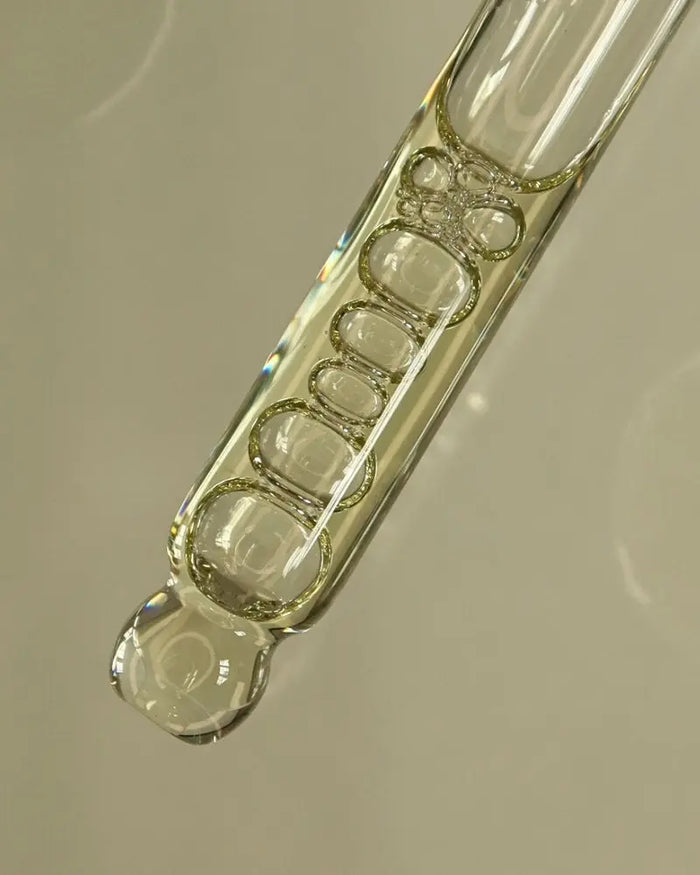 Close-up of a glass vial with a clear liquid on a neutral background