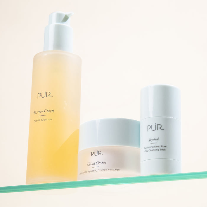 PÜR skincare trio on a glass shelf featuring Forever Clean Cleanser, Cloud Cream Moisturizer, and Joystick Exfoliating Cleansing Stick.