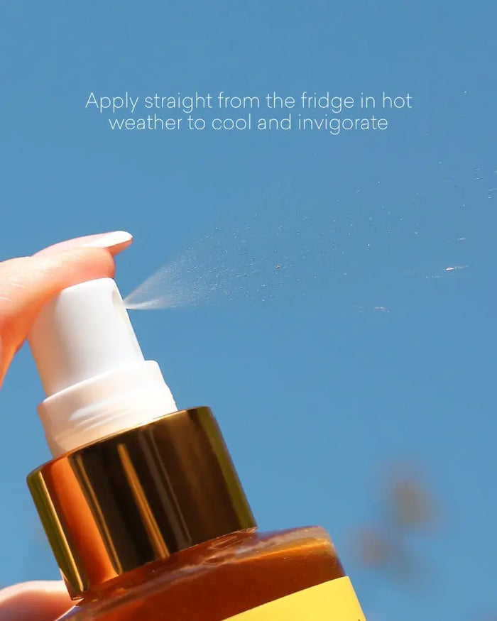 Hand holding a spray bottle with a blue sky background. The product is being spritzed.