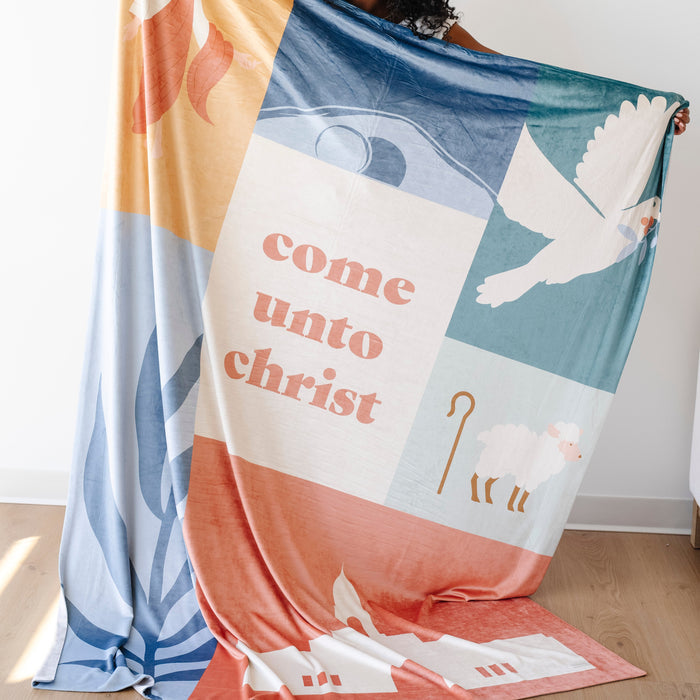 Person holding a Come Unto Christ LDS blanket featuring faith-centered illustrations of Jesus Christ, a dove, shepherd imagery, and uplifting Christian artwork, meaningful blanket for LDS youth and missionaries.