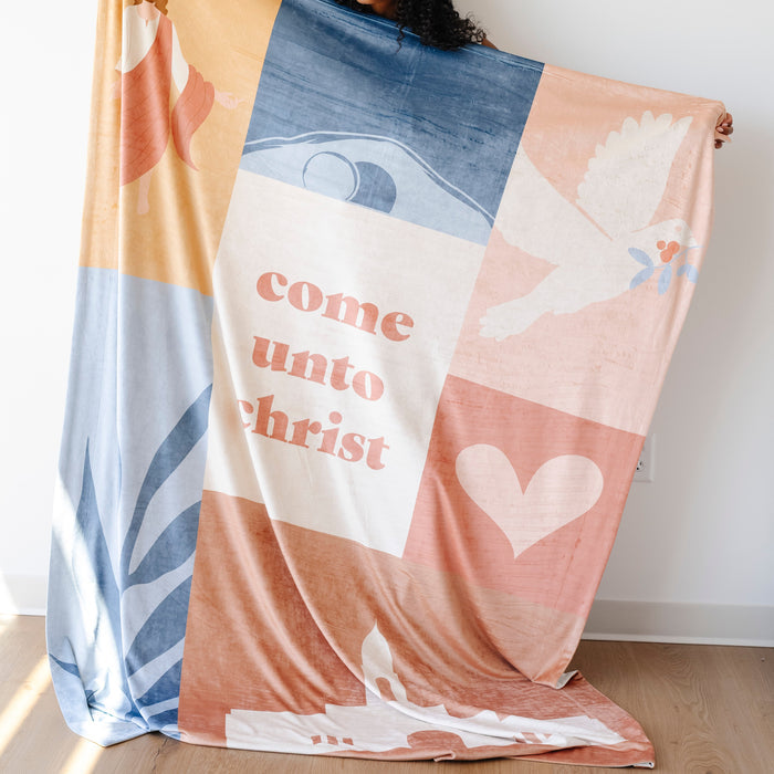 Person holding a Come Unto Christ LDS blanket featuring pastel faith-centered artwork, a dove, heart, and the words "Come Unto Christ," meaningful blanket for LDS youth, girls camp, youth conference, and Christian homes.