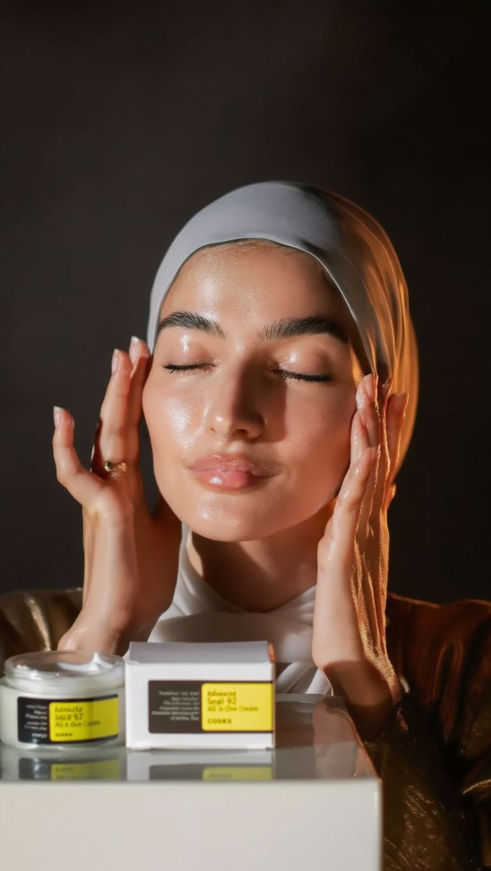 Woman applying cream to her face with skincare products on a dark background