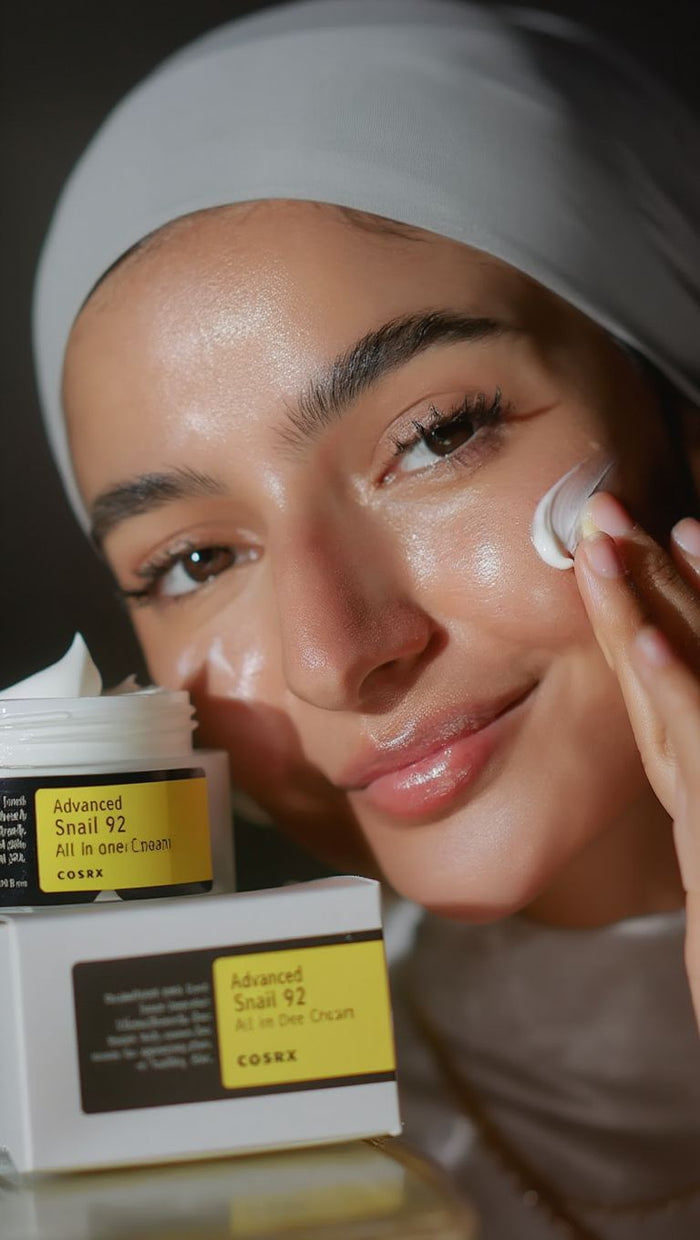 Woman applying cream to her face with aCosrx product in the foreground