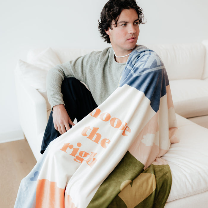 Boy sitting on a couch wrapped in a Christian baptism blanket featuring the CTR design, temple artwork, and Choose the Right message.