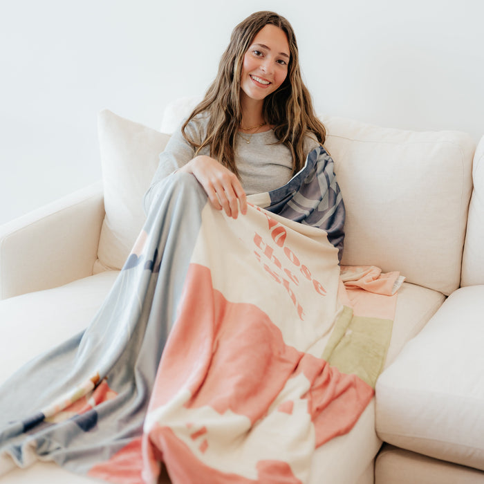 Girl sitting on a couch wrapped in a Christian blanket featuring the CTR Baptism design, celebrating faith and the covenant of baptism.