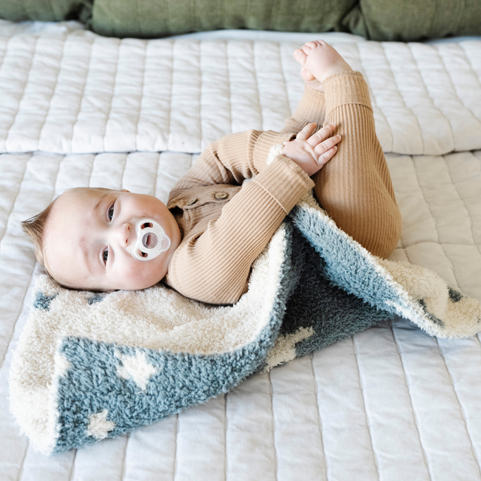 A happy baby boy with a double-layer Bamboni® baby blanket. The plush, breathable blanket features a two-tone blue and cream star design, offering ultimate softness and warmth. Made from Saranoni’s signature stretchy, cloud-like Bamboni® fabric, this luxury baby blanket provides comfort for naps, tummy time, and on-the-go snuggles. The perfect blend of warmth and breathability, it’s a must-have for parents seeking high-quality, ultra-soft blankets. The soft blanket is a mini blanket and Saranoni