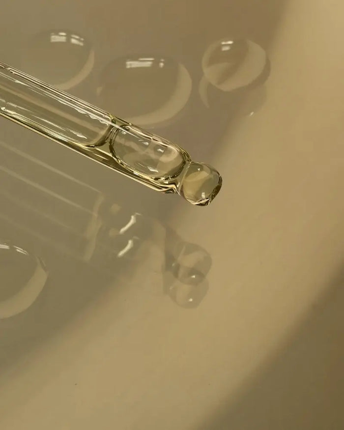 Close-up of a glass dropper with liquid on a reflective surface
