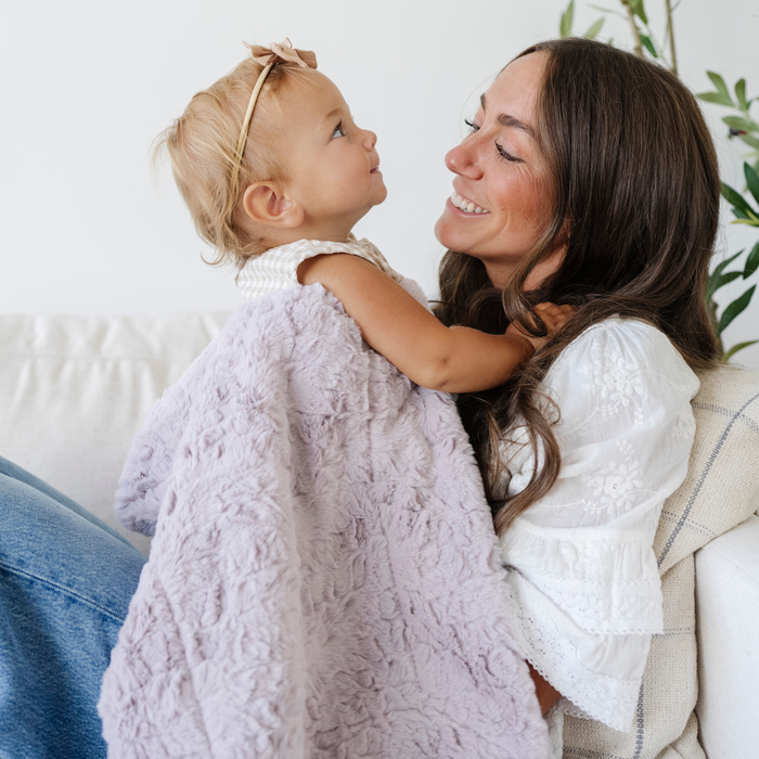 Mom holding baby girl snuggled with a purple soft receiving baby blanket.