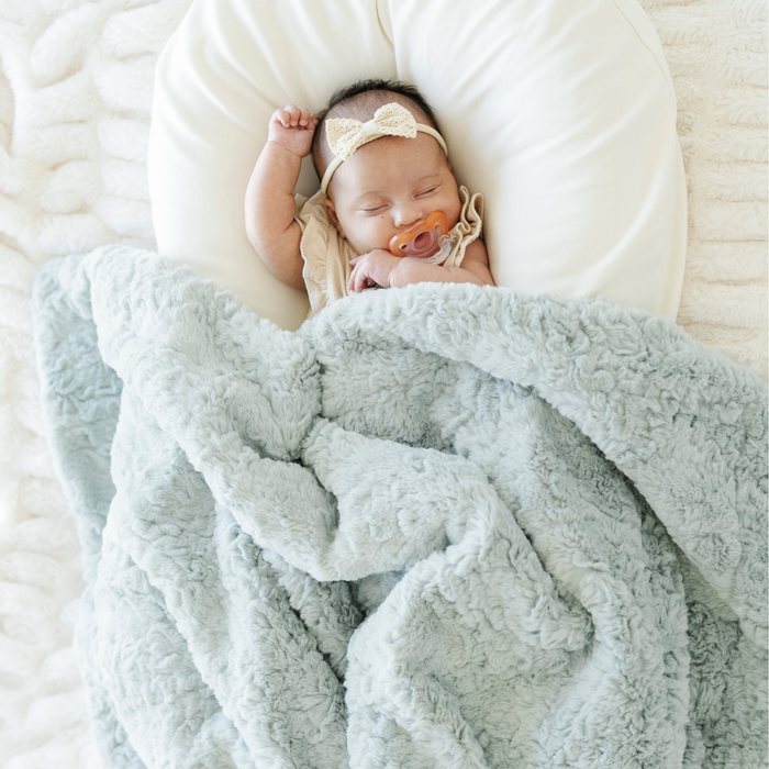Baby girl sleeping with a mint green dream faux fur receiving blanket next to her.
