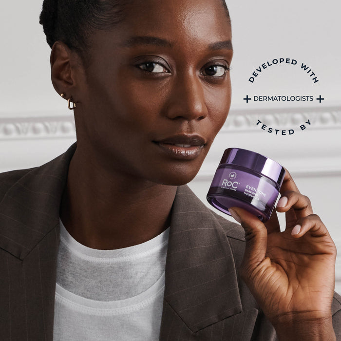 Woman holding a purple jar of Roc cream against a neutral background