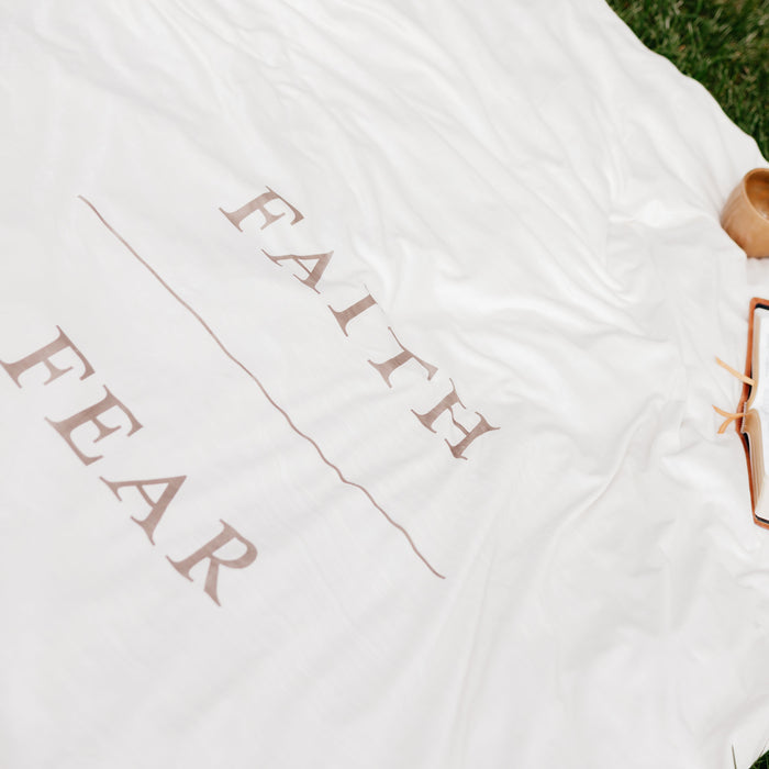 Shell cream Christian blanket displayed on grass featuring the words "Faith Over Fear," faith-inspired throw blanket offering comfort, encouragement, and a reminder to trust God through life's challenges.