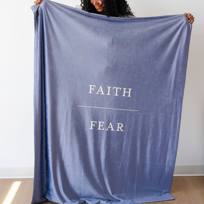 Person holding a harbor blue Christian blanket featuring the words "Faith Over Fear," faith-inspired throw blanket offering comfort, encouragement, and a reminder to trust God through life's challenges.