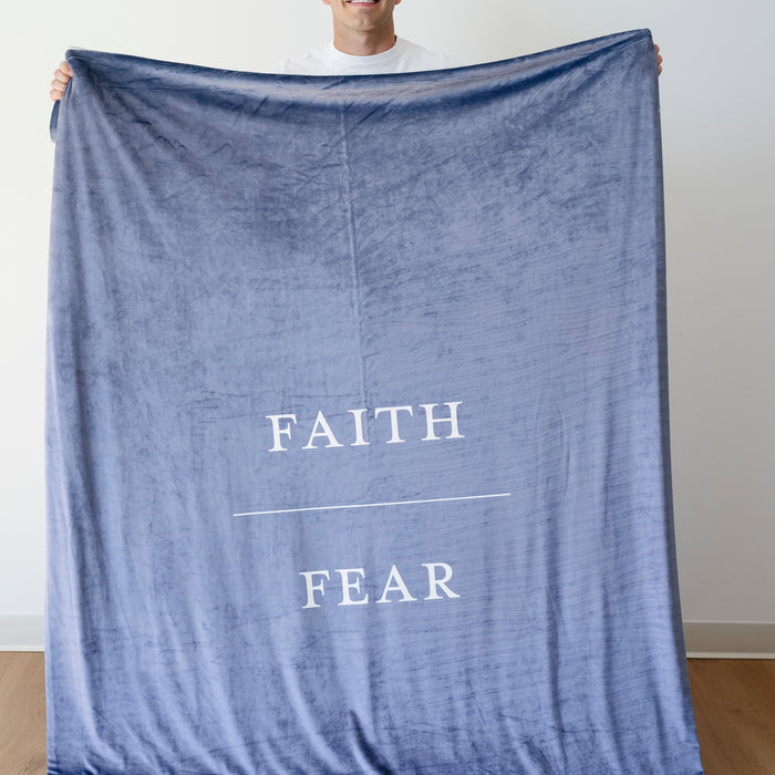 Person holding a harbor blue Christian blanket featuring the words "Faith Over Fear," faith-inspired throw blanket offering comfort, encouragement, and a reminder to trust God through life's challenges.