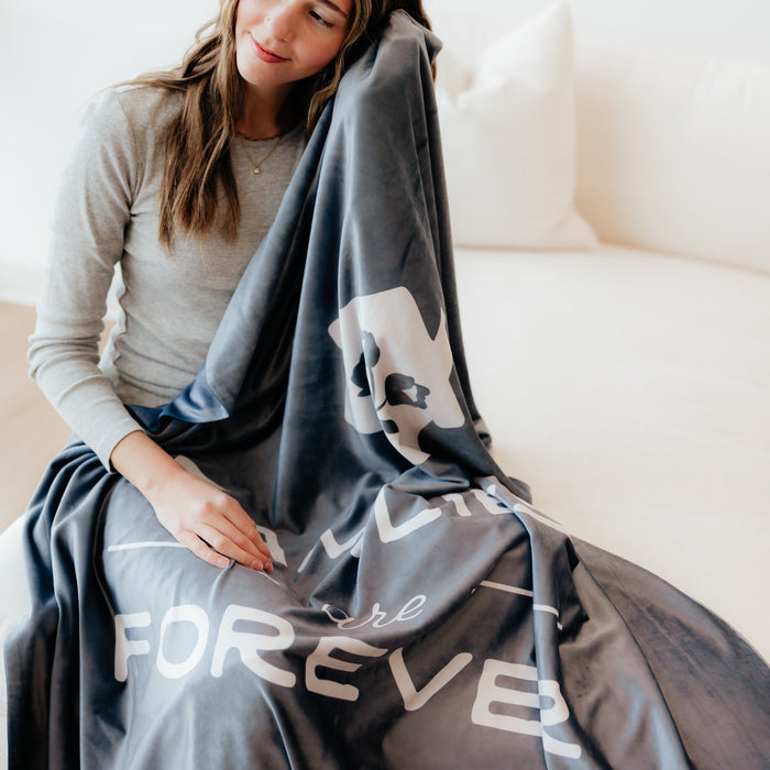 Woman relaxing on a couch wrapped in a dark obsidian LDS blanket featuring the words "Families Are Forever," soft faith-inspired throw blanket celebrating eternal families and meaningful connections.