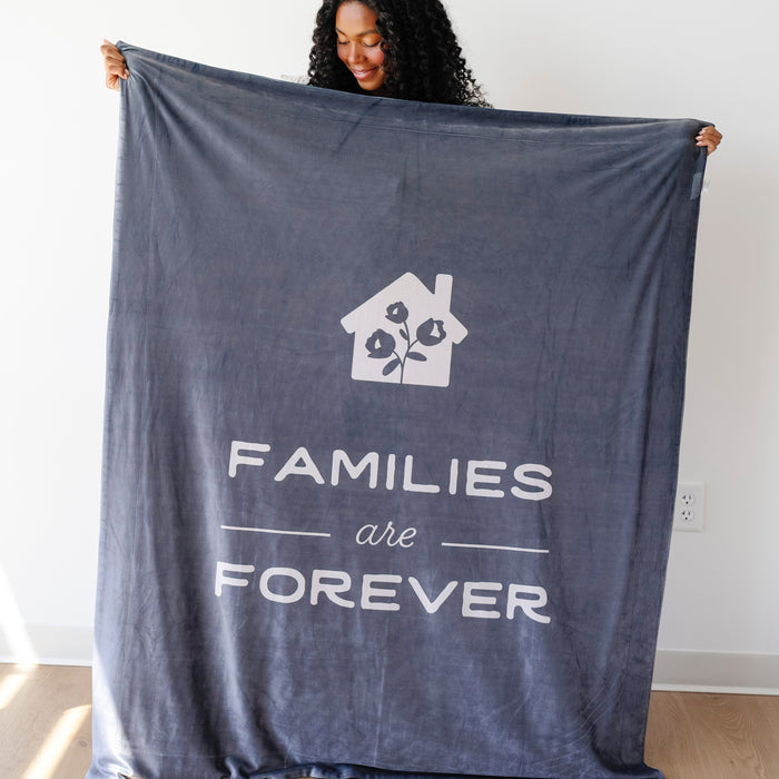 Person holding a dark obsidian LDS blanket featuring the words "Families Are Forever" and a home design, soft faith-inspired throw blanket celebrating eternal families.