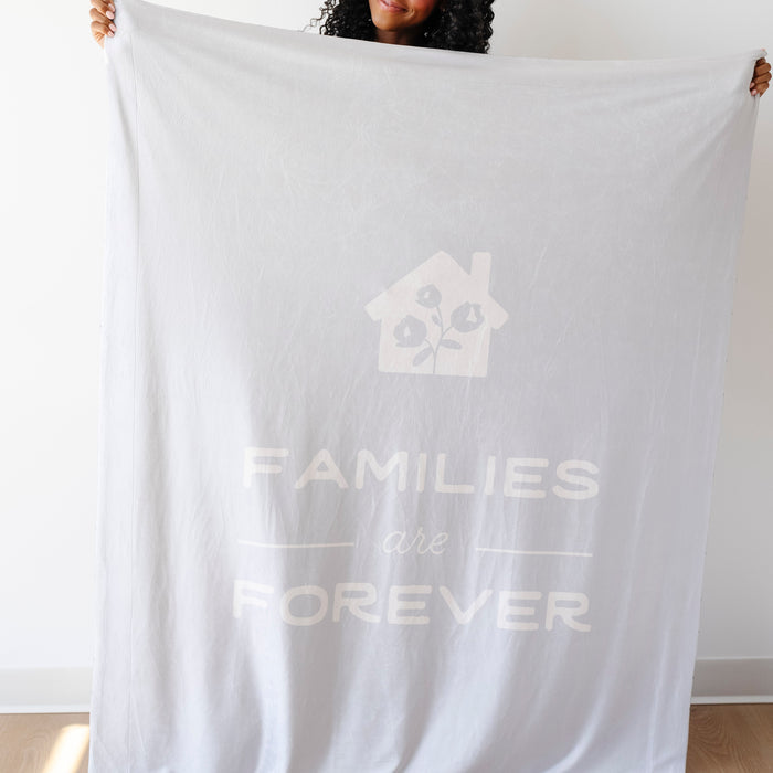 Person holding a light glacier blue LDS blanket featuring the words "Families Are Forever" and a home design, soft faith-inspired throw blanket celebrating eternal families and lasting connections.