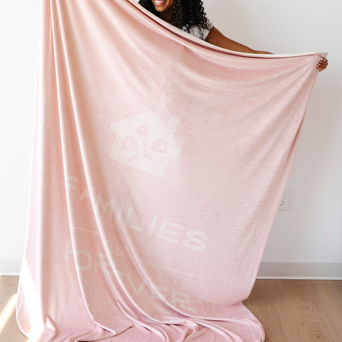 Person holding a soft peony pink LDS blanket featuring the words "Families Are Forever" and a home design, faith-inspired throw blanket celebrating eternal families and lasting connections.