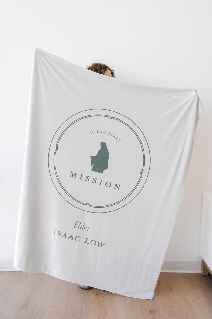 Person holding a soft sage green personalized missionary blanket featuring custom missionary details and mission-inspired artwork.