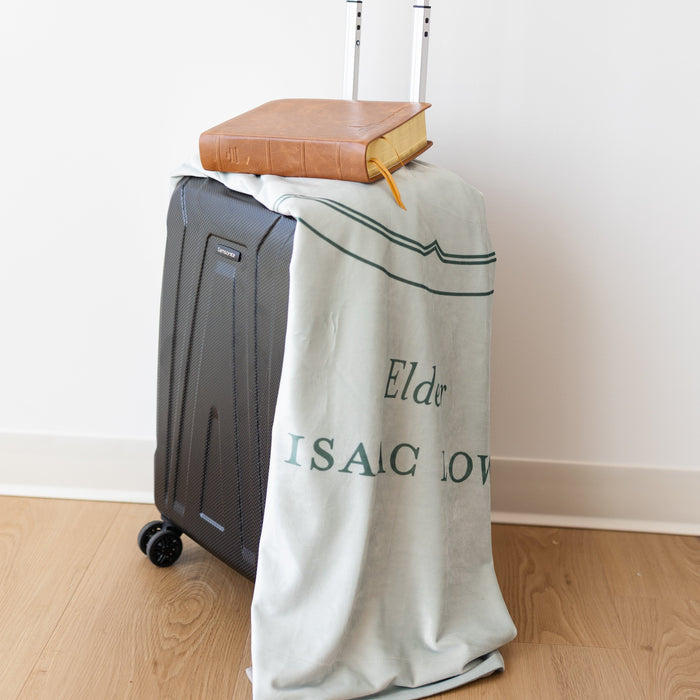 Personalized In His Service missionary blanket displayed with luggage and scriptures, featuring custom missionary details and faith-centered design.