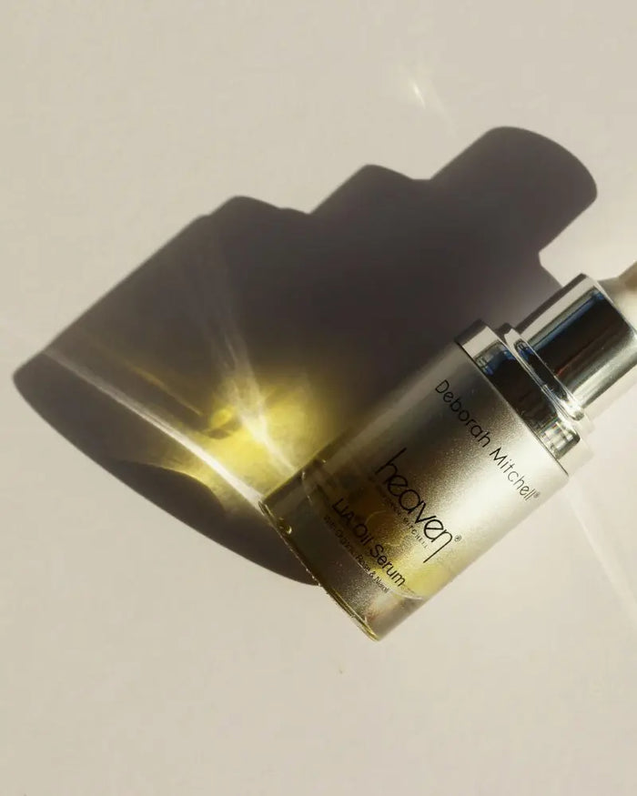 LIA Oil Serum bottle lay flat on an off-white background. The light reflects off the product bottle creating a warm glow.