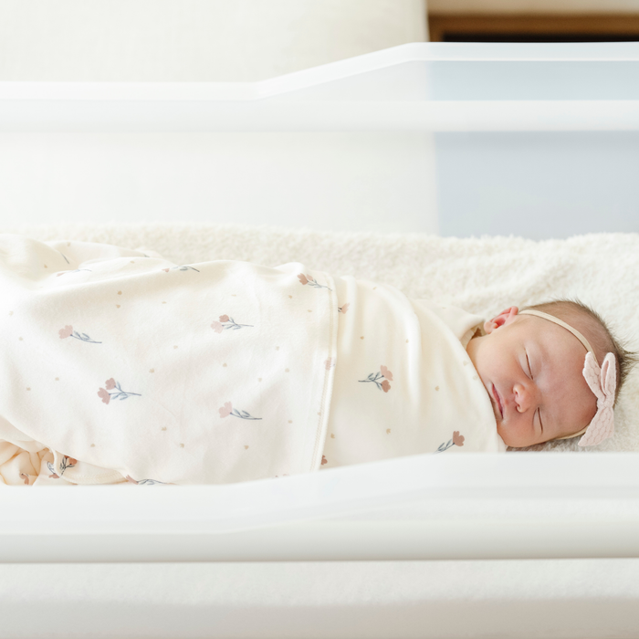 A newborn baby girl is swaddled in a floral minky stretch luxe swaddle.
