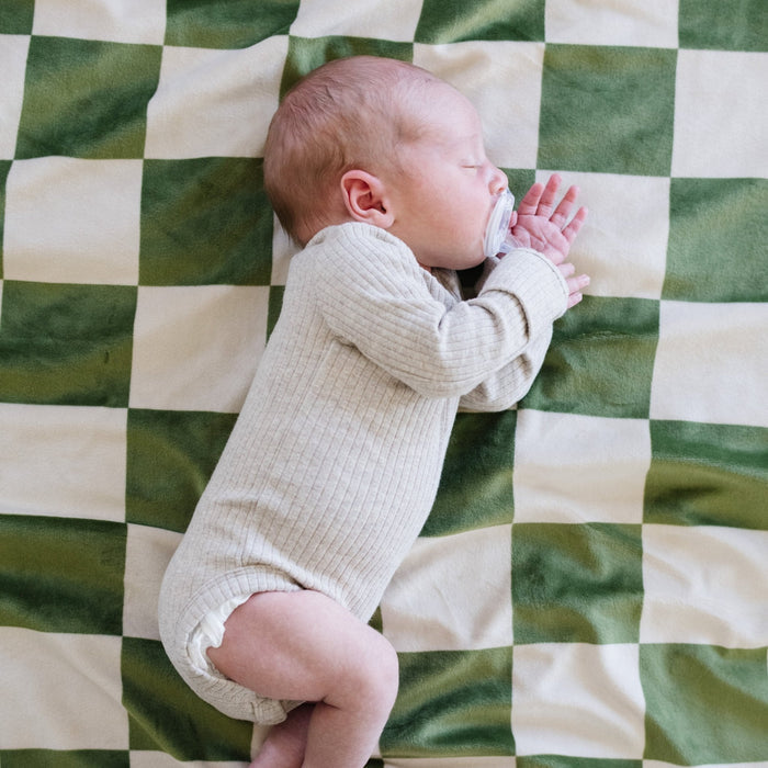 A baby boy sleeping on a olive and cream checkered minky stretch blanket. The soft blanket is a luxury blanket and a Saranoni blanket. This cozy blanket is also a receiving blanket and is a cute and cozy baby blanket. This stretchy blanket is a great nursery item.