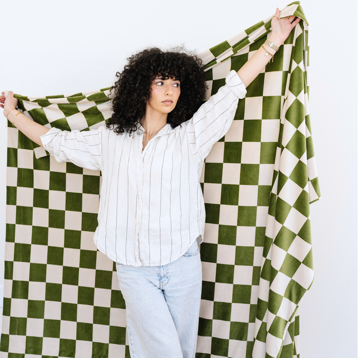 Woman stands holding a Olive and Cream checkered minky stretch XL blanket.