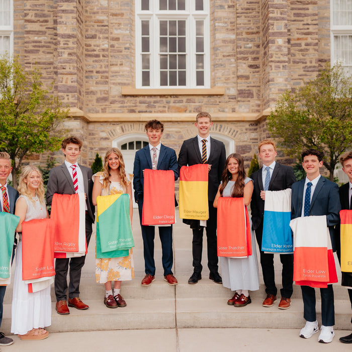 Group of missionaries standing outside a templeholding personalized mission flag blankets, custom LDS missionary keepsake blankets for mission farewells and homecomings.