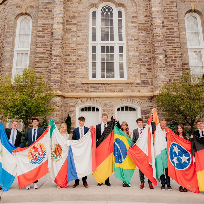 Group of missionaries holding personalized mission flag blankets in front of a church building, custom LDS missionary keepsake blankets celebrating mission calls, farewells, and service.