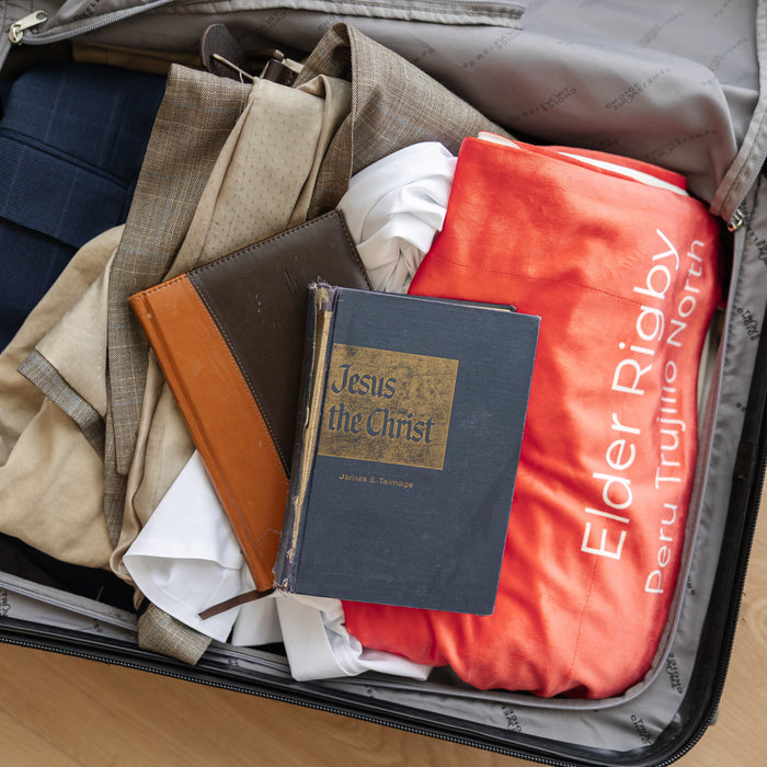 Open suitcase packed for missionary service with a personalized mission flag blanket and scriptures, custom LDS missionary keepsake blanket for mission preparation, travel, and meaningful gifts.