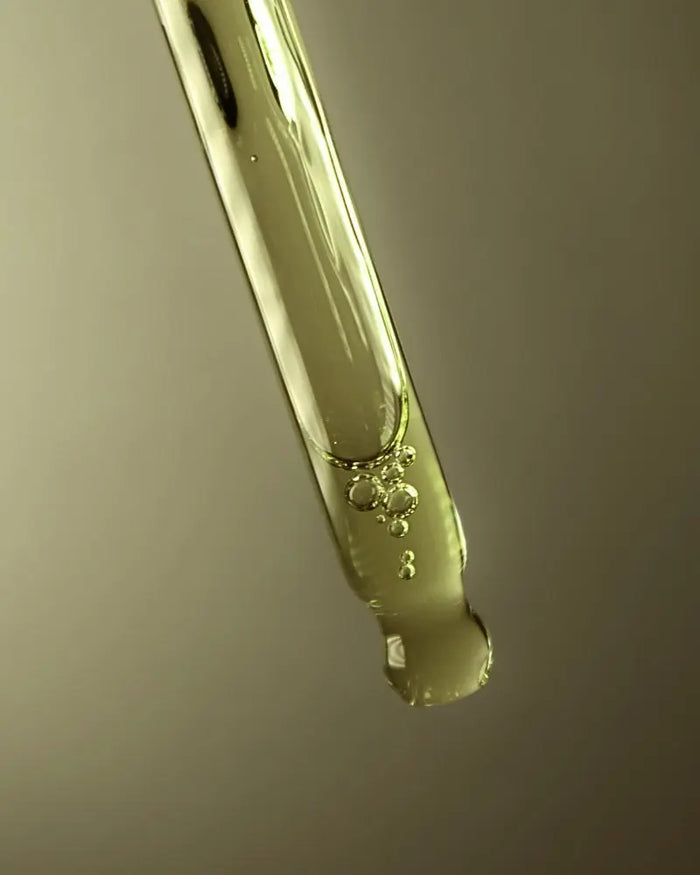 Close-up of a dropper with a clear liquid against a neutral background
