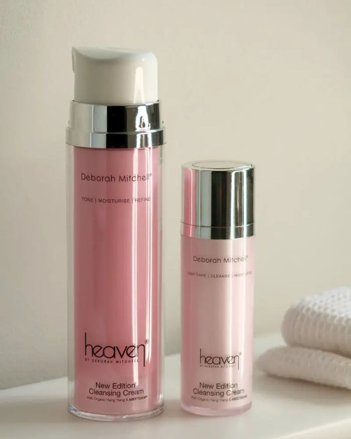 Two pink skincare bottles with silver caps on a light surface. Showing the large and small version of the product. In the background are some folded up waffle towels.