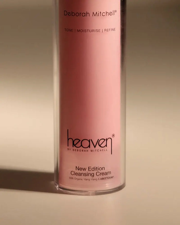 Pink bottle of New Edition Cleansing Cream. On beige background.