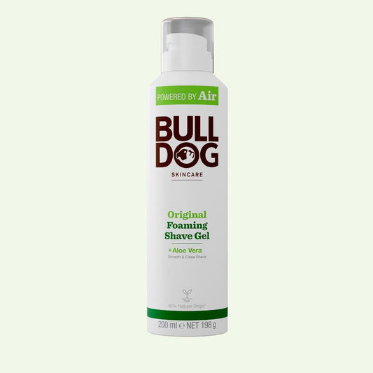 A white can of Original Foaming Shave Gel stands upright on a pale green background, featuring green and brown text and highlighting aloe vera and natural origin ingredients for a smooth, close shave.
