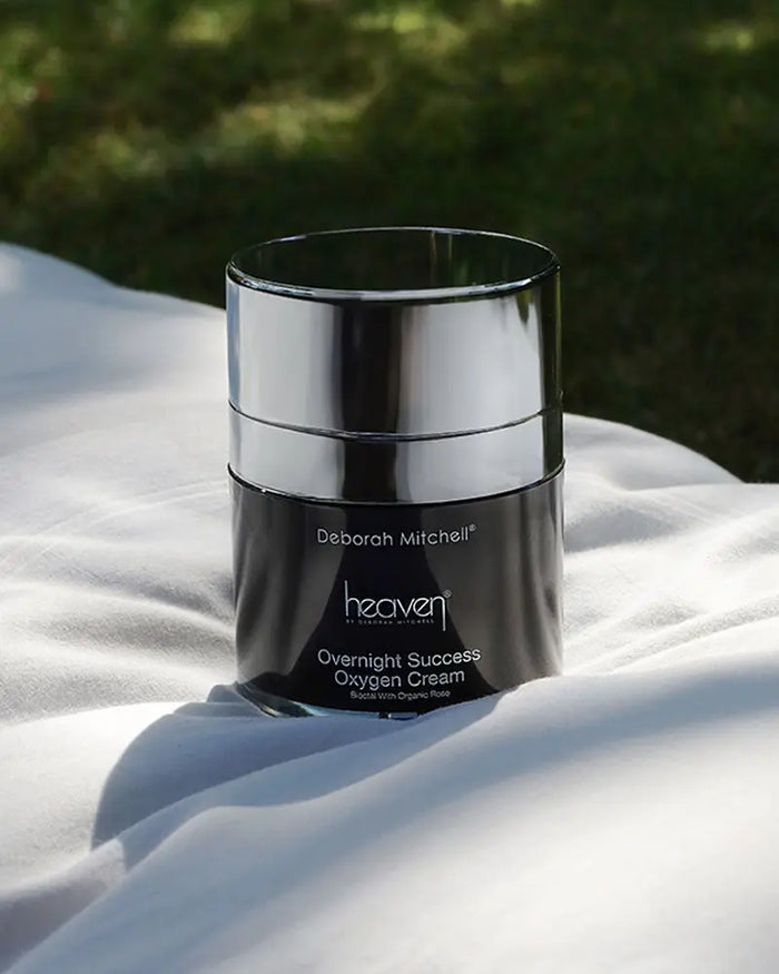 Black cream jar labeled 'Deborah Mitchell heaven' on a white surface with greenery in the background