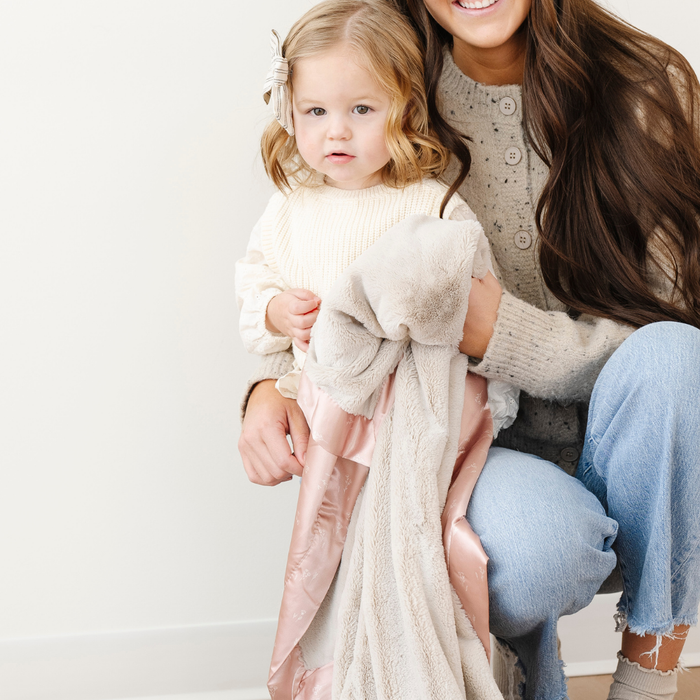 A little girl holds a toddler blanket that is a light tan blanket with a floral satin border. This soft blanket is a luxury blanket and a Saranoni blanket. This toddler blanket is a great little girl gift or addition to a kid's bedroom.