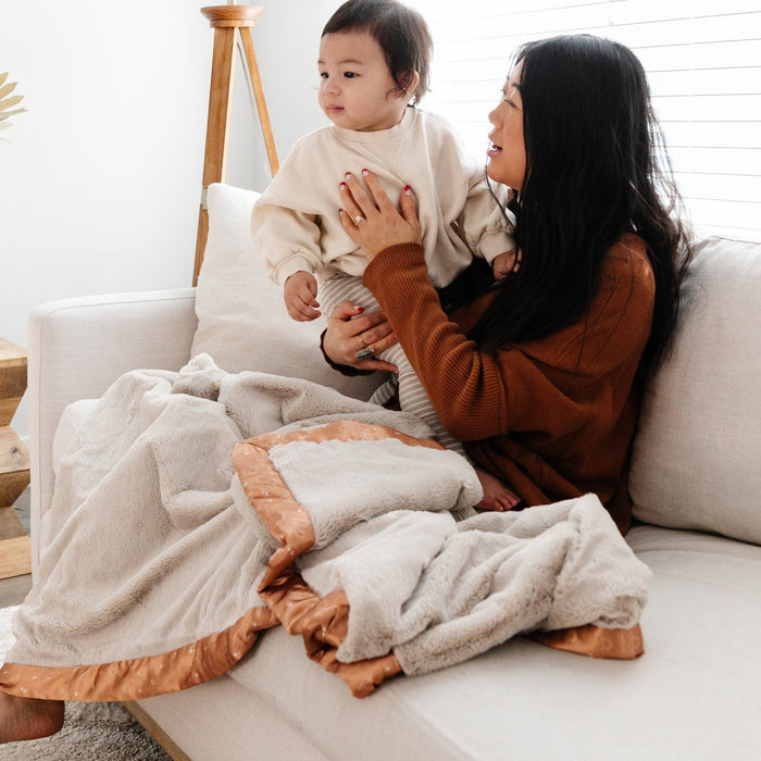 Mom and daughter snuggling on couch with a cozy and soft tan toddler blanket.